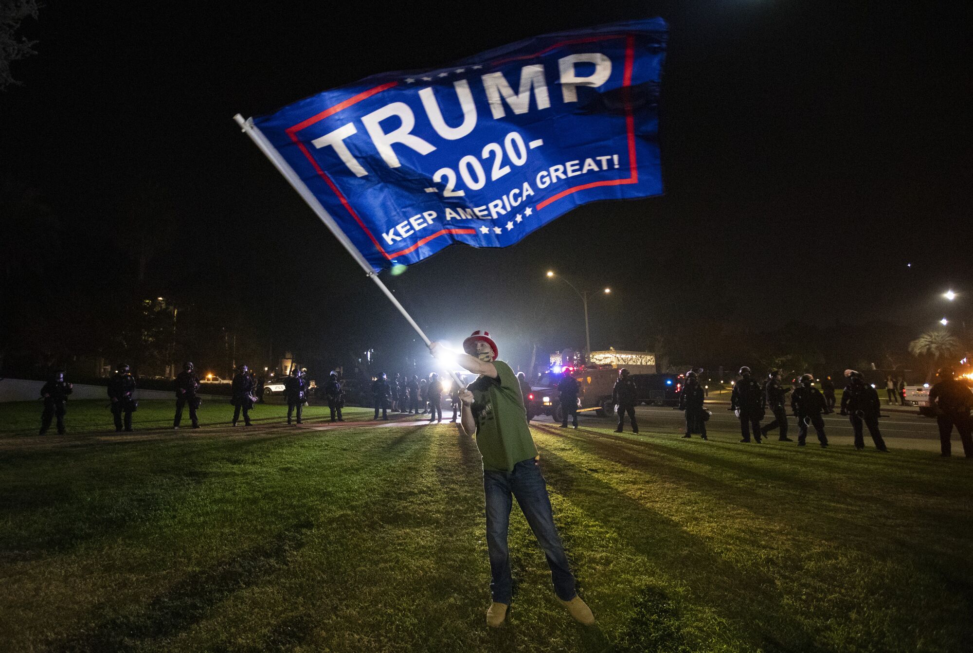 A Trump supporter waves a Trump 2020 flag in front of a line of Beverly Hills police on Tuesday night. 
