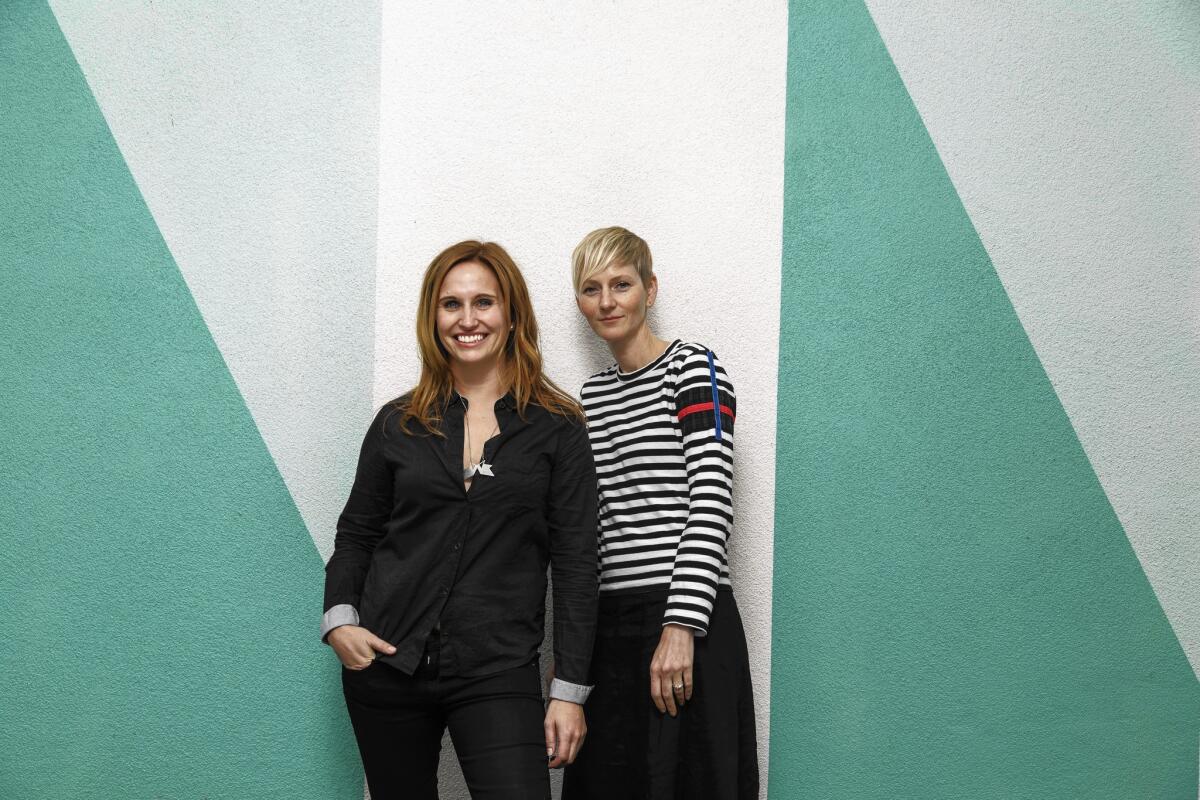 Catherine Johnson and Rebecca Rudolph stand before a green and white color-blocked wall.