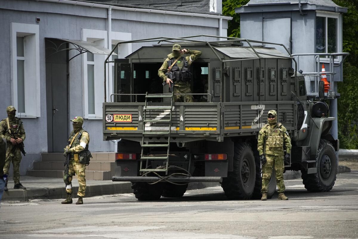 Russian soldiers stand in or near a military vehicle on a street.