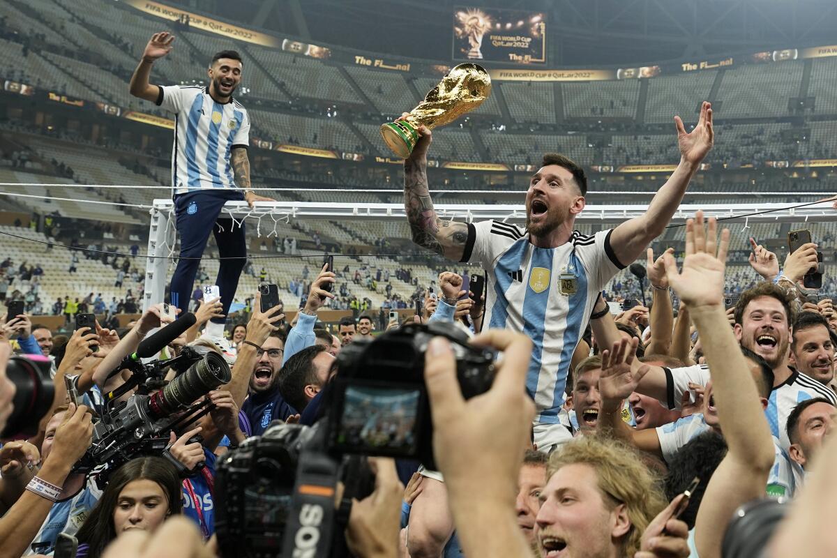 Argentina's Lionel Messi holds up a trophy while being held up amid a crowd of people in a stadium.