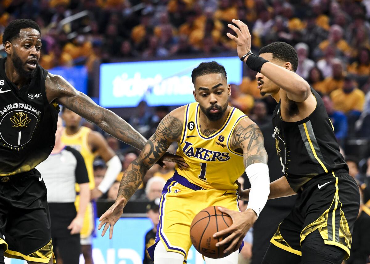 Lakers guard D'Angelo Russell drives between Golden State's JaMychal Green and Jordan Poole.