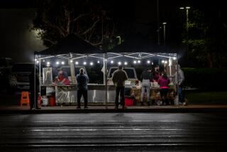 SANTA ANA, CA - DECEMBER 27, 2022: Customers wait in line on a rain slicked evening for warm food from a street vendor on the sidewalk off McFadden Avenue on December 27, 2022 in Santa Ana, California.The City of Santa Ana is cracking down on unlicensed street vendors in the city. In the past two months, the city has shut down 100 of the businesses temporarily. The businesses were back up within a few days moving to different locations. (Gina Ferazzi / Los Angeles Times)