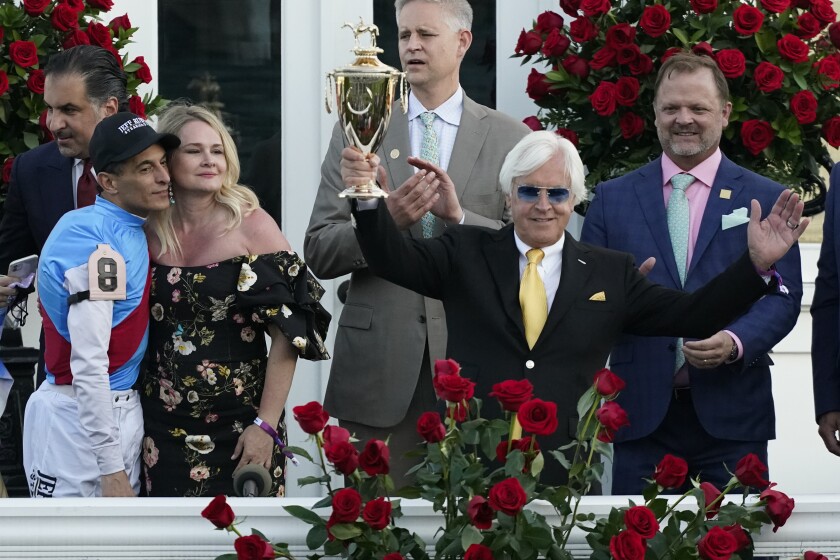 FILE - Jockey John Velazquez, front left, stands with Jill Baffert as they watch as Jill's husband, trainer Bob Baffert, holds up the winner's trophy after their victory with Medina Spirit in the 147th running of the Kentucky Derby at Churchill Downs in Louisville, Ky. Medina Spirit was stripped of the victory in last year’s Kentucky Derby and Mandaloun was declared the winner in a ruling by state racing stewards on Monday, Feb. 21, 2022. (AP Photo/Jeff Roberson, FIle)