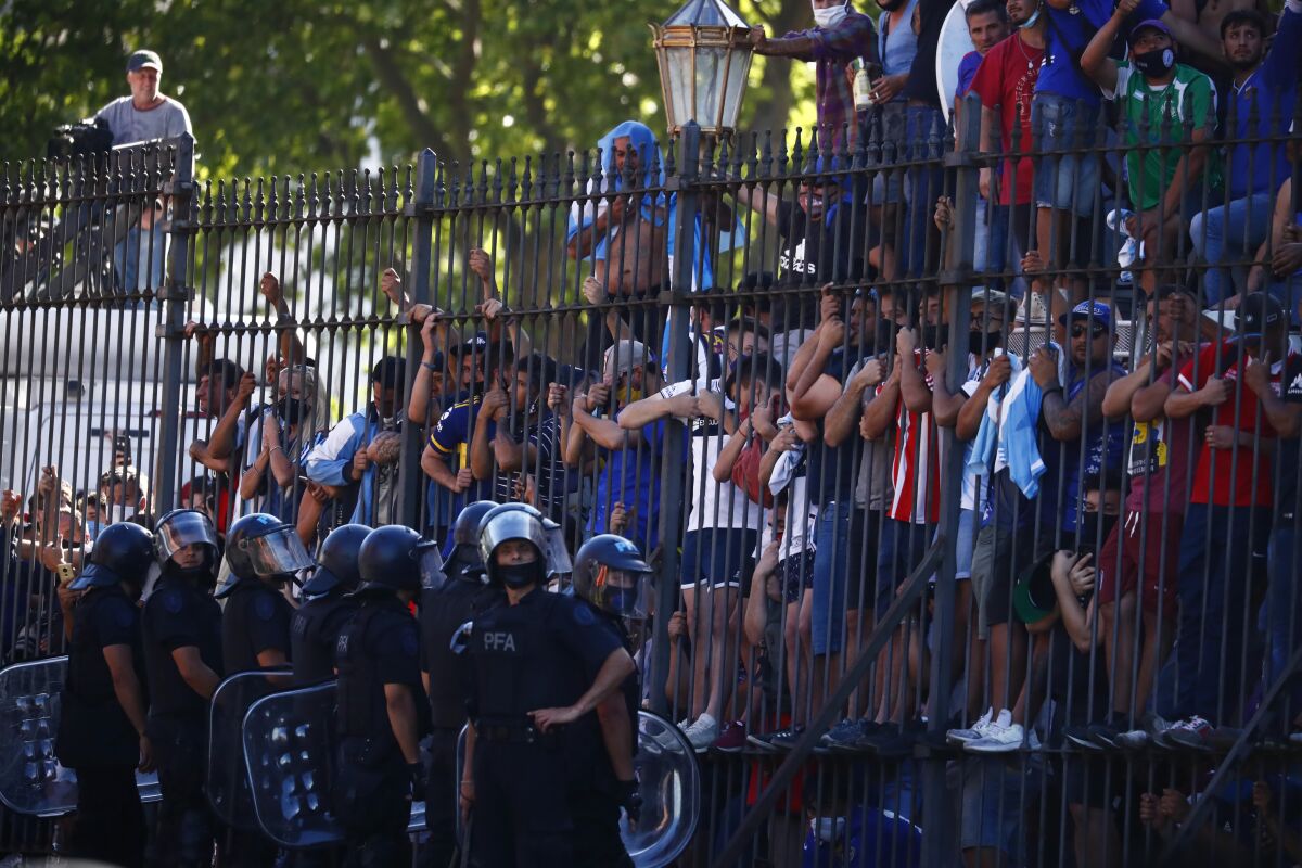Mourning fans climb the fence of the presidential palace to get a glimpse of the casket carrying Diego Maradona's body.
