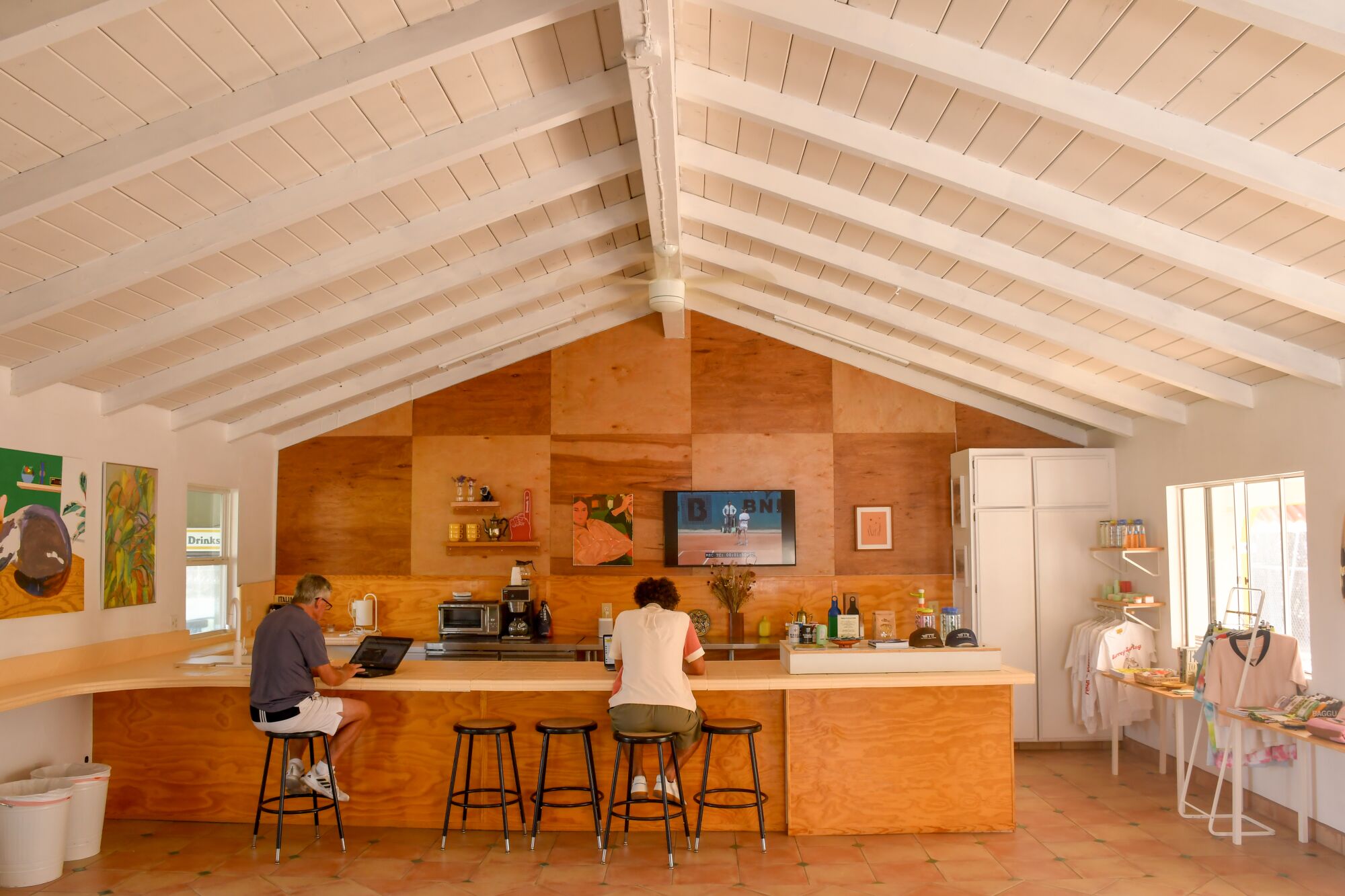 Two people sit on barstools at a kitchen counter in a small building with a pointed roof.