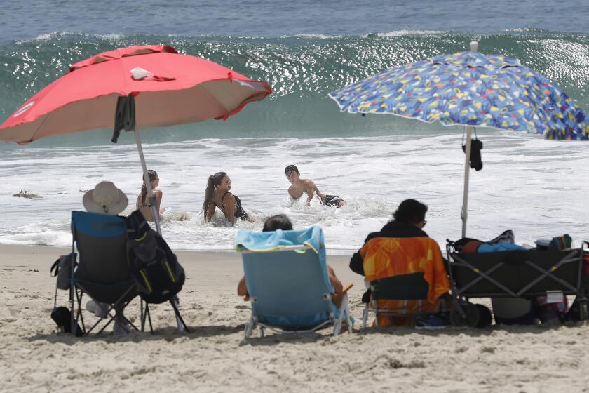 Beachgoers play in the shore break near their umbrellas on a warm afternoon at Laguna's Main Beach on Tuesday.