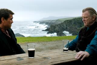 Colin Farrell and Brendan Gleeson staring at each other across a picnic table with beer glasses on it overlooking the sea