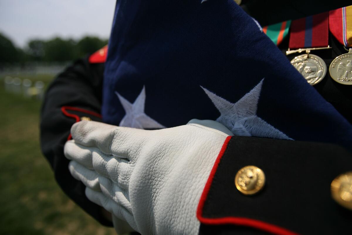 A Marine solemnly holds a folded American flag at a graveside memorial service.