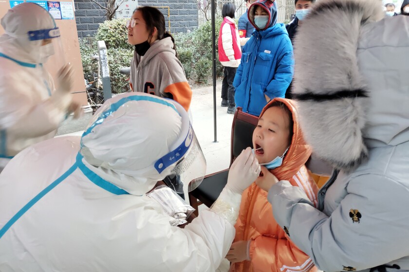 A medical worker wearing a protective suit swabs a child for a coronavirus test in Huaxian County in central China's Henan Province, Friday, Jan. 14, 2022. China further tightened its anti-pandemic measures in Beijing and across the country on Friday as scattered outbreaks continued ahead of the opening of the Winter Olympics in a little over two weeks. (Chinatopix via AP)