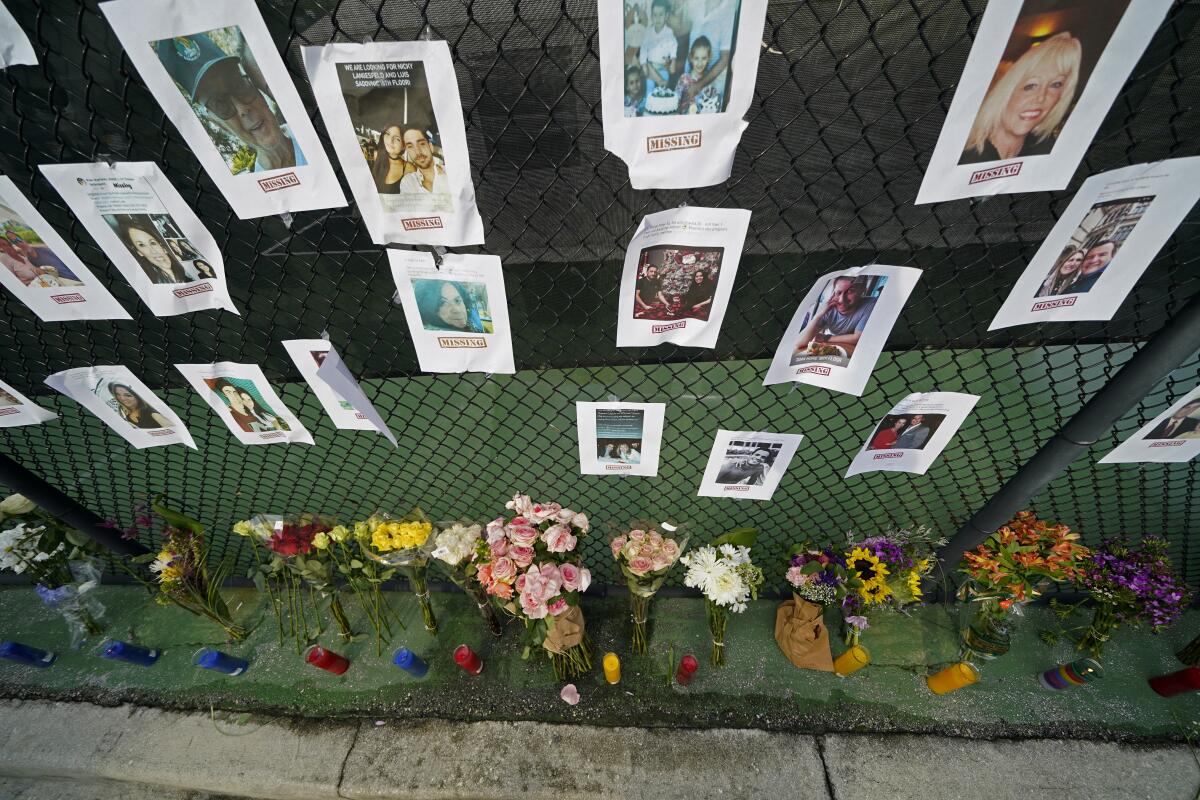 Photos of the missing hang from a chain-link fence above flowers and candles