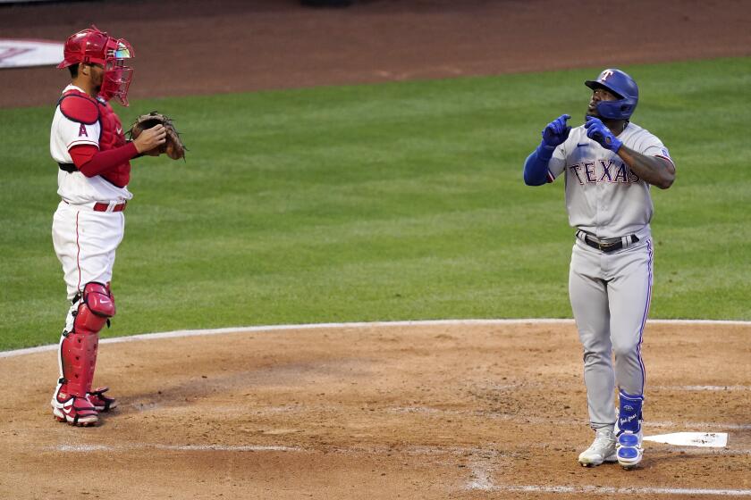 Texas Rangers' Adolis Garcia, right, celebrates as he scores after hitting a solo home run as Los Angeles Angels catcher Kurt Suzuki watches during the third inning of a baseball game Monday, April 19, 2021, in Anaheim, Calif. (AP Photo/Mark J. Terrill)