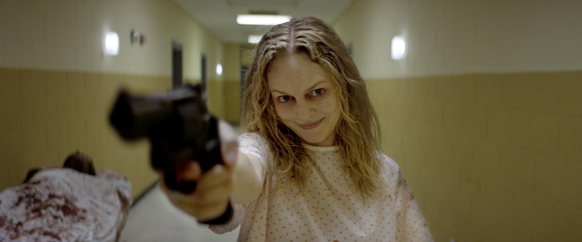 A smiling woman points a gun down a hallway.