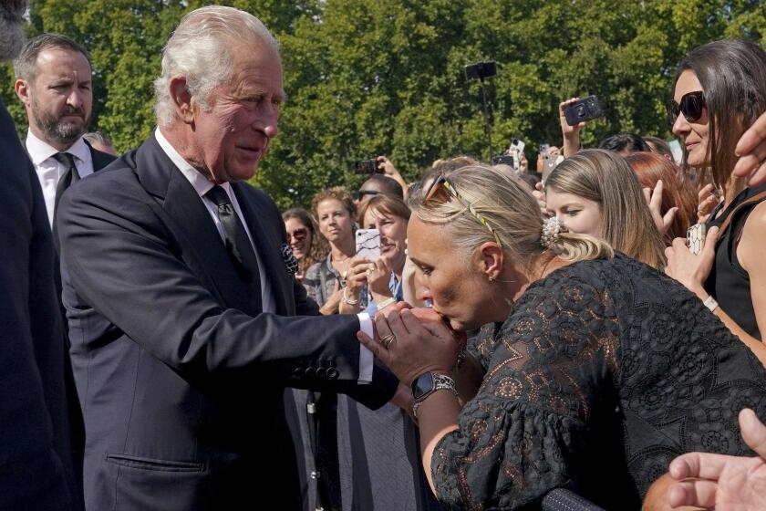 A well-wisher kisses the hand of Britain's King Charles III as he walks outside at Buckingham Palace following Thursday's death of Queen Elizabeth II, in London, Friday, Sept. 9, 2022. King Charles III, who spent much of his 73 years preparing for the role, planned to meet with the prime minister and address a nation grieving the only British monarch most of the world had known. He takes the throne in an era of uncertainty for both his country and the monarchy itself. (Yui Mok/Pool Photo via AP)