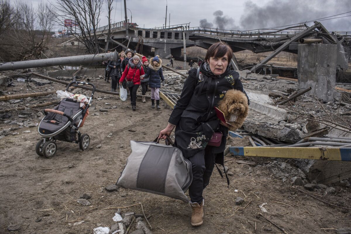 People cross an improvised path under a destroyed bridge while fleeing the town of Irpin, Ukraine, Sunday, March 6, 2022. In Irpin, near Kyiv, a sea of people on foot and even in wheelbarrows trudged over the remains of a destroyed bridge to cross a river and leave the city. (AP Photo/Oleksandr Ratushniak)