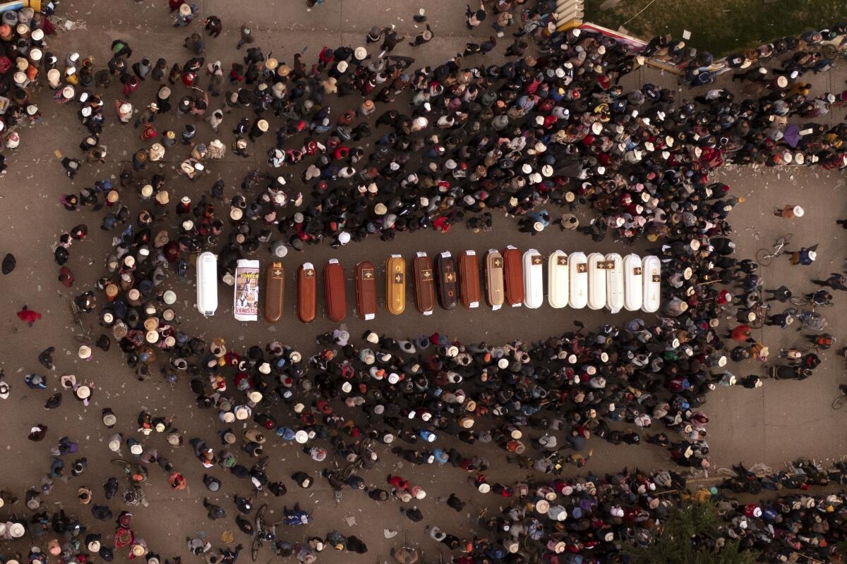 An aerial view of people standing around a row of coffins.