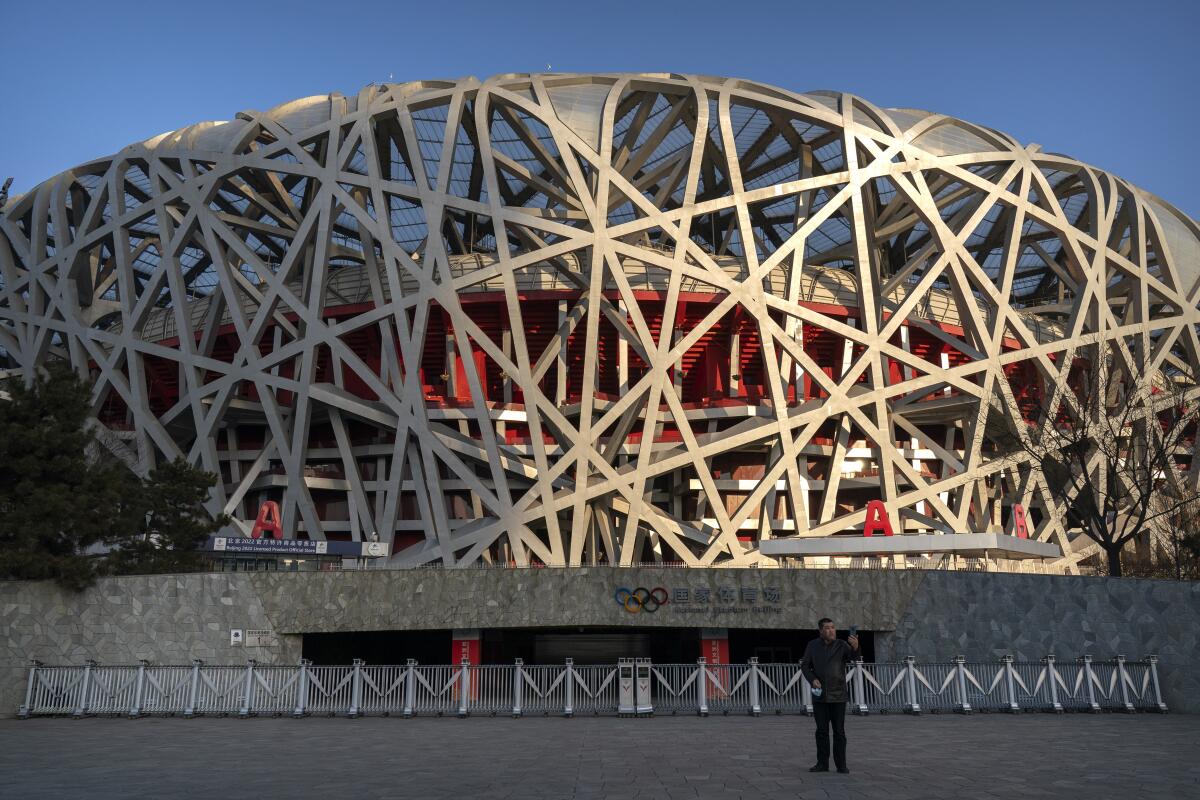 A man poses for a selfie near the Olympic logo at the National Stadium, also known as the Bird's Nest, in Beijing, Tuesday, Feb. 2, 2021. The venue will host the opening and closing ceremonies during the upcoming 2022 Beijing Winter Olympics. (AP Photo/Mark Schiefelbein)