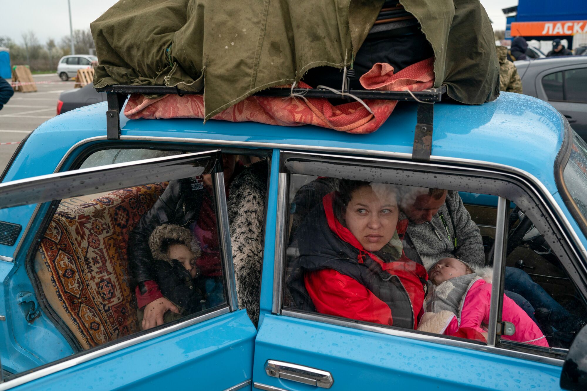Adults and children in a car with belongings packed on top.