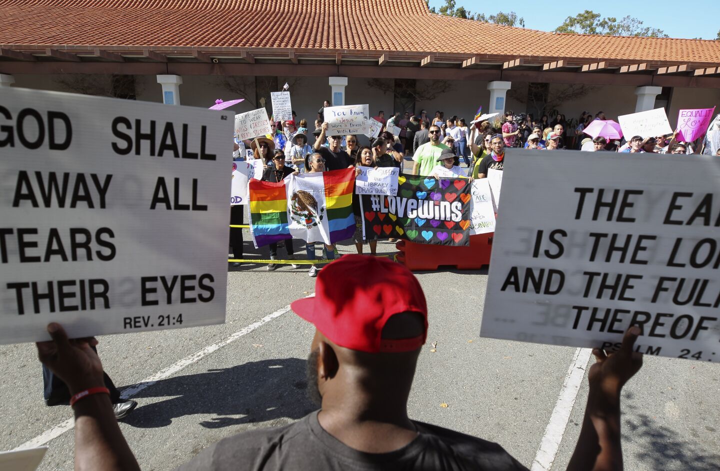 James Smith holds signs as he stands with protesters against the Drag Queen Story Hour while those in support of stories being read to children by drag queens chant slogans on the other side of a barrier at the Chula Vista Public Library Civic Center Branch on Tuesday, September 10, 2019 in Chula Vista, California.