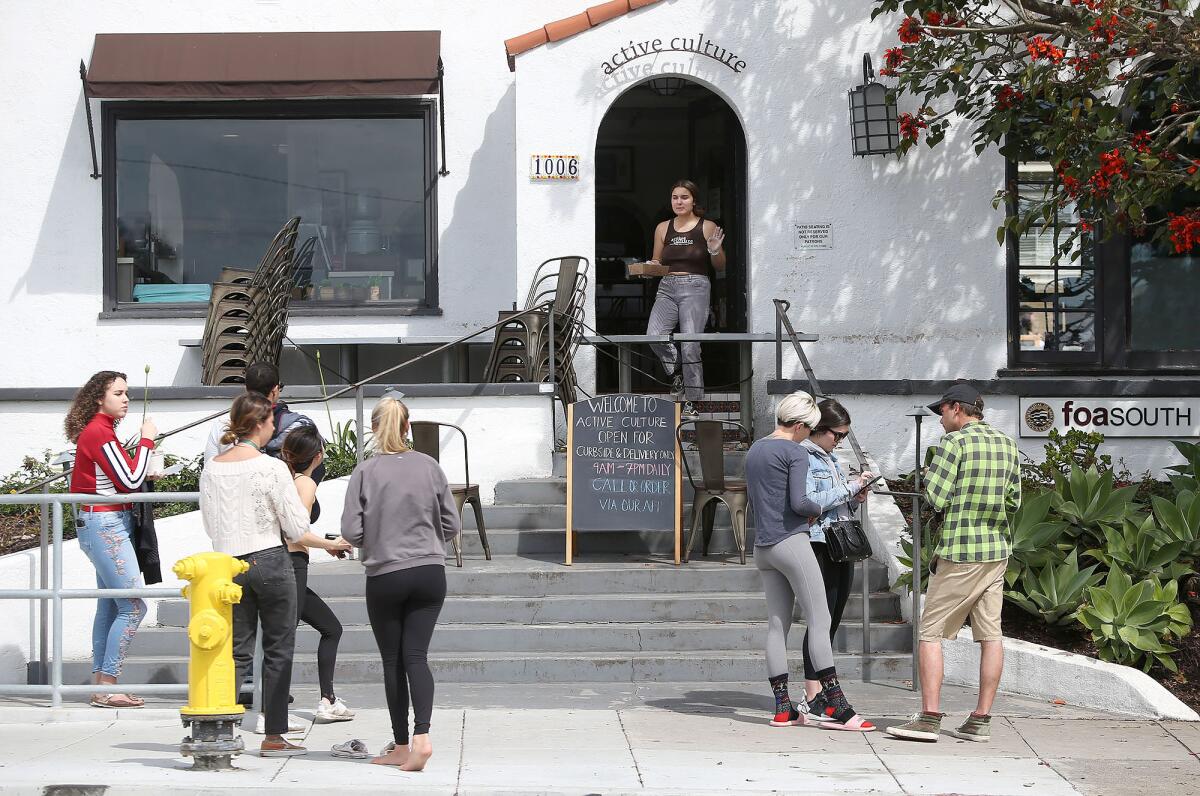 Small groups wait on the sidewalk for phone-in, pick-up orders at Active Culture in Laguna Beach on March 19.