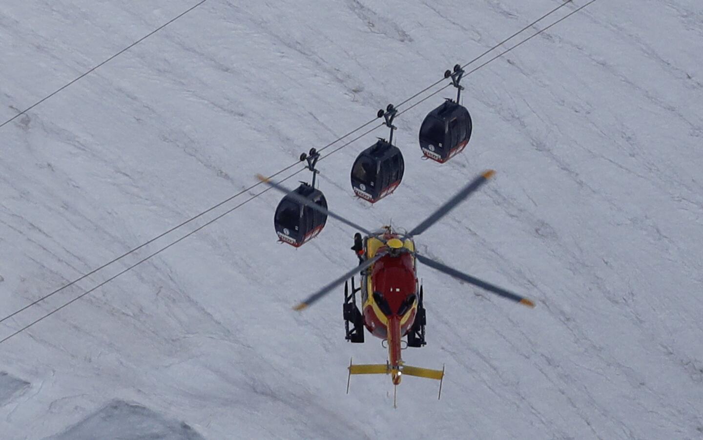 An EC-135 helicopter operated by the French Societe Civile hovers near three stuck cable cars.