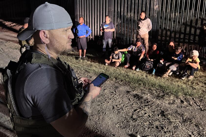 EAGLE PASS TEXAS APRIL 12, 2022 - Samuel Hall, 40, North Texas-based founder of the Patriots for America militia, surveys a group of migrants stopped by U.S. Customs and Border Protection agents after crossing the Rio Grande in Eagle Pass, Texas, last month. (Molly Hennessy-Fiske / Los Angeles Times)