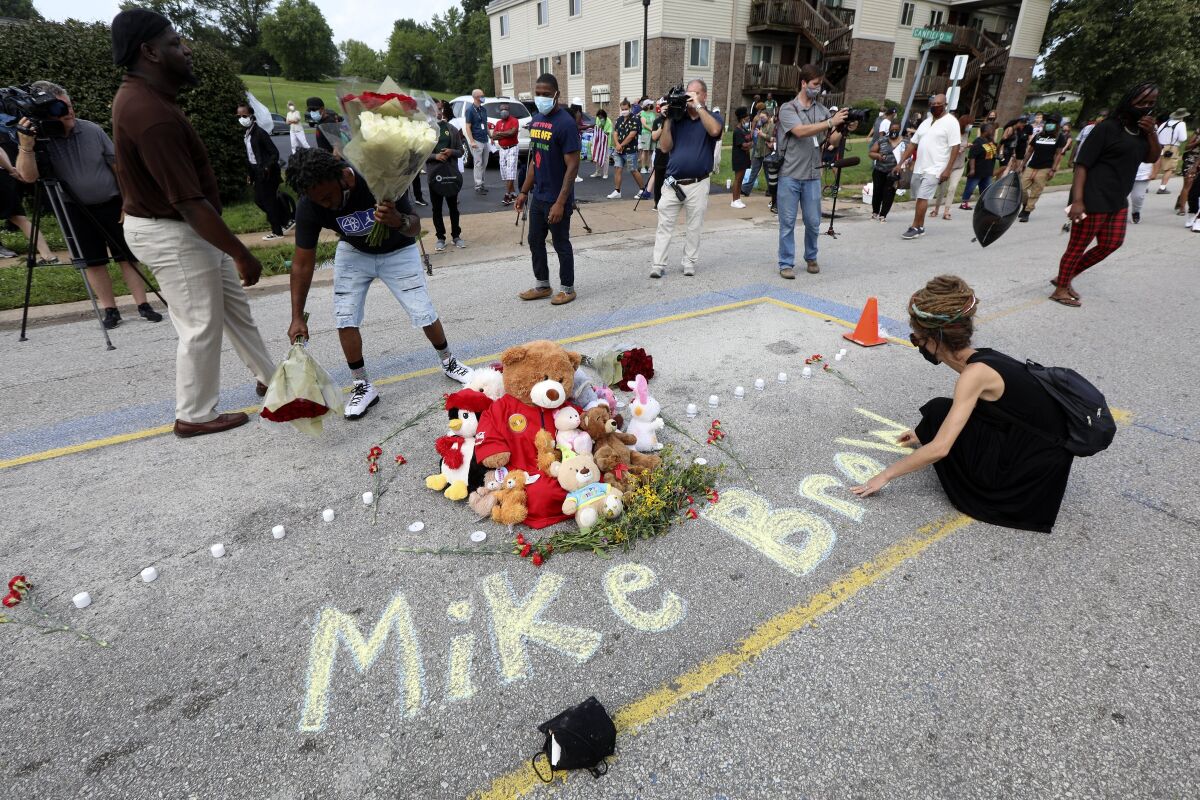 Frontline protester Jazz chalks up a message on the pavement before the start of a memorial service for Michael Brown at the Pleasant View Gardens Apartments, formerly known as the Canfield Green Apartments, on the seventh anniversary of the police shooting of Brown on Monday, Aug. 9, 2021 in Ferguson, Mo. (Laurie Skrivan/St. Louis Post-Dispatch via AP)