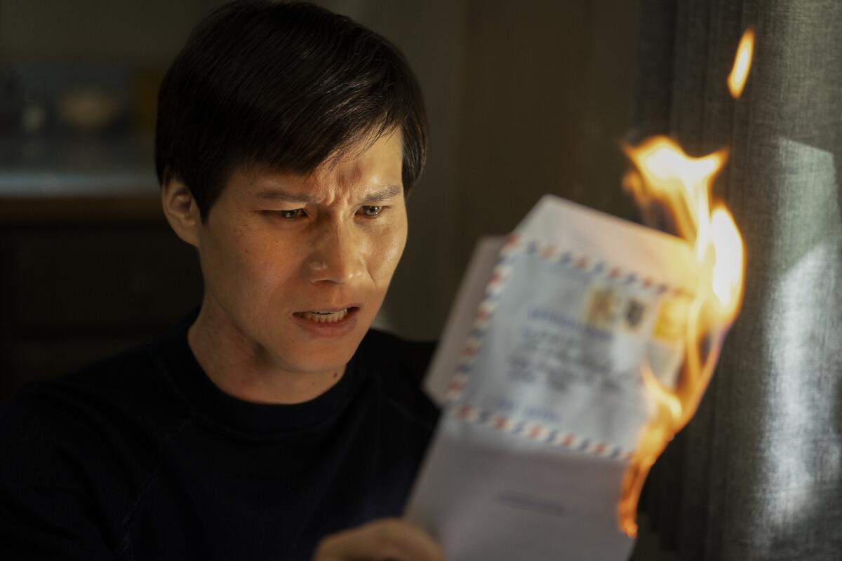 A man in black shirt holds up a letter that is on fire.