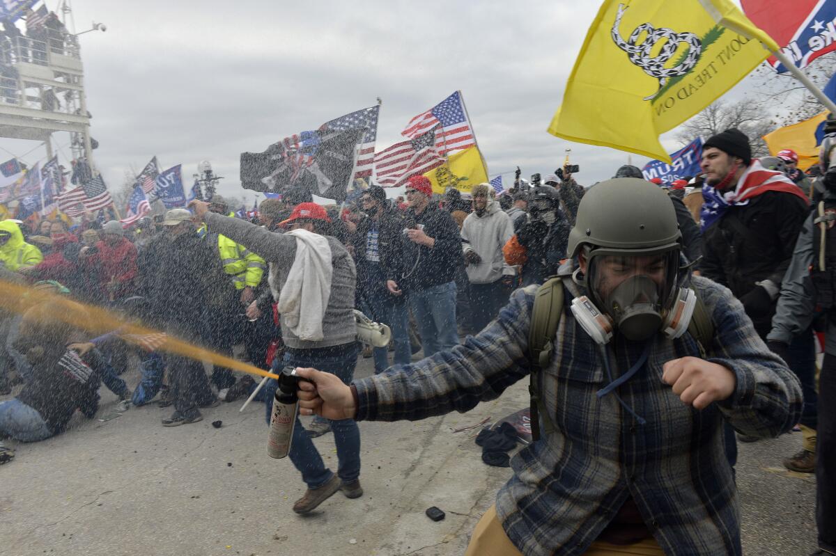 A man sprays Mace with a crowd of pro-Trump rioters behind him