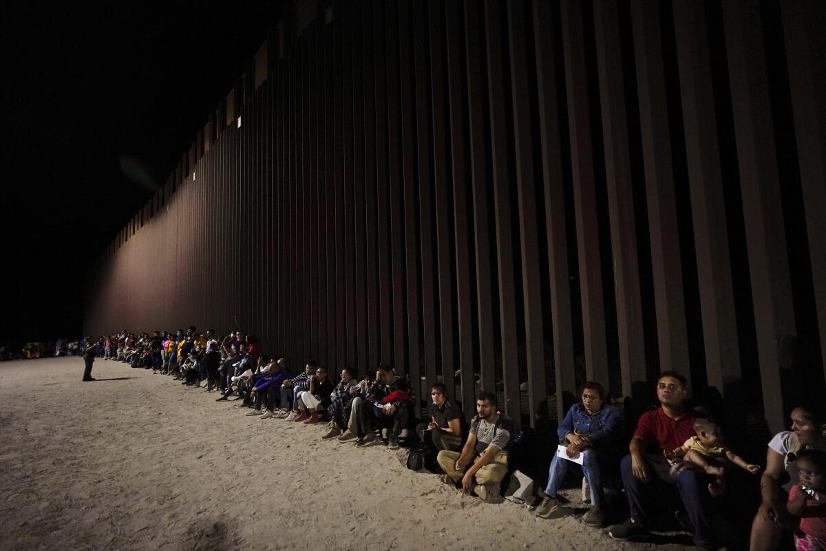 Migrantes esperan junto a un muro fronterizo el 23 de agosto del 2022, tras cruzar desde México cerca de Yuma, 