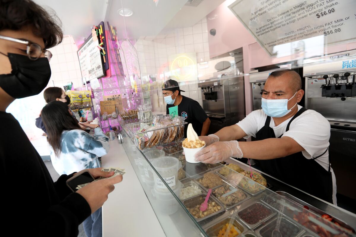 A person in gloves and a face mask handing a bowl of frozen yogurt over the counter to another person in a face mask