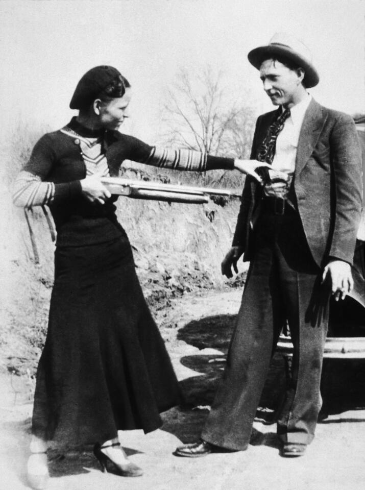 Bonnie Parker aims a shotgun at her partner, Clyde Barrow while clowning beside an automobile in 1932.