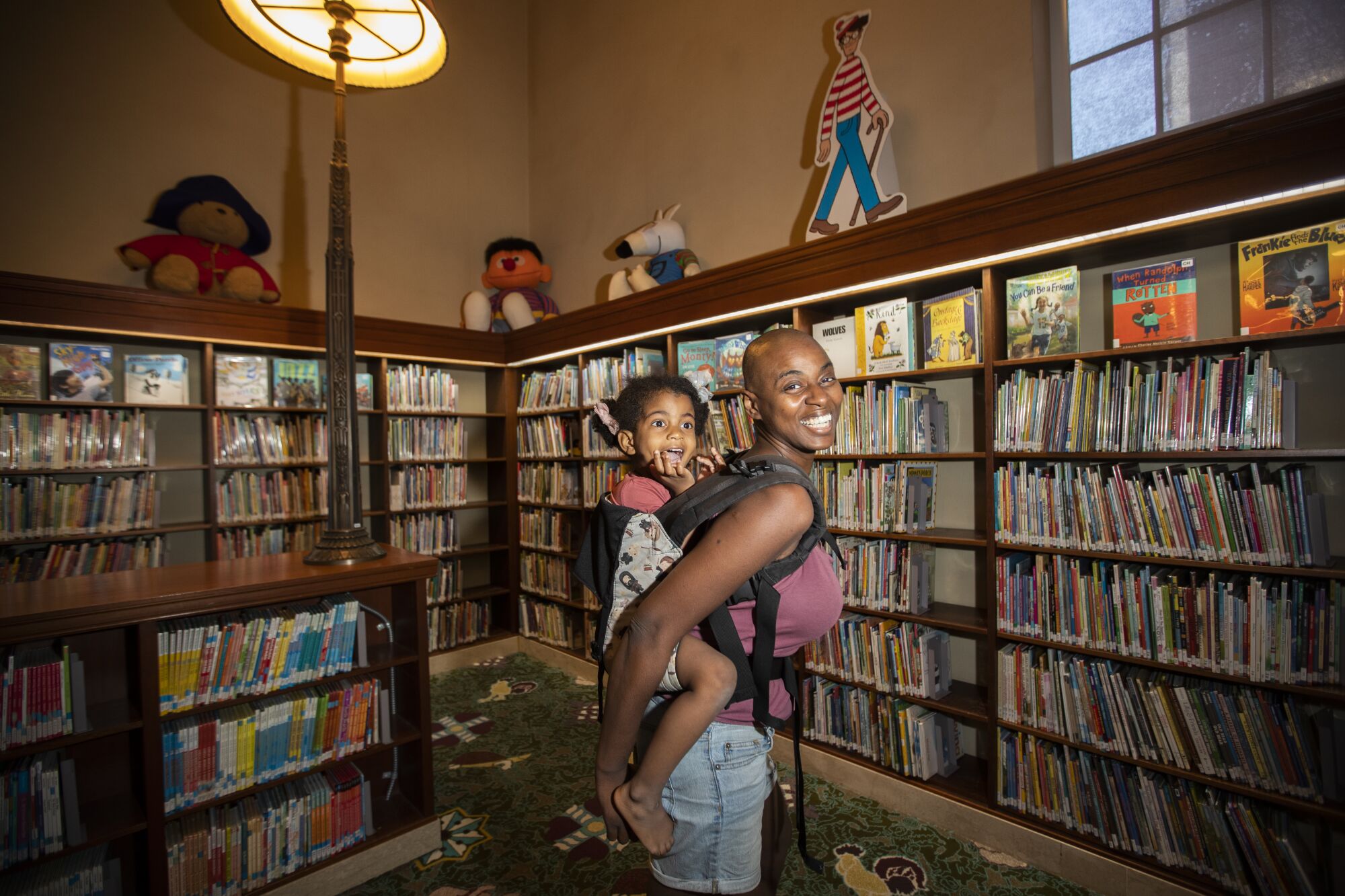 A woman carrying her daughter on her back amid walls of bookshelves.