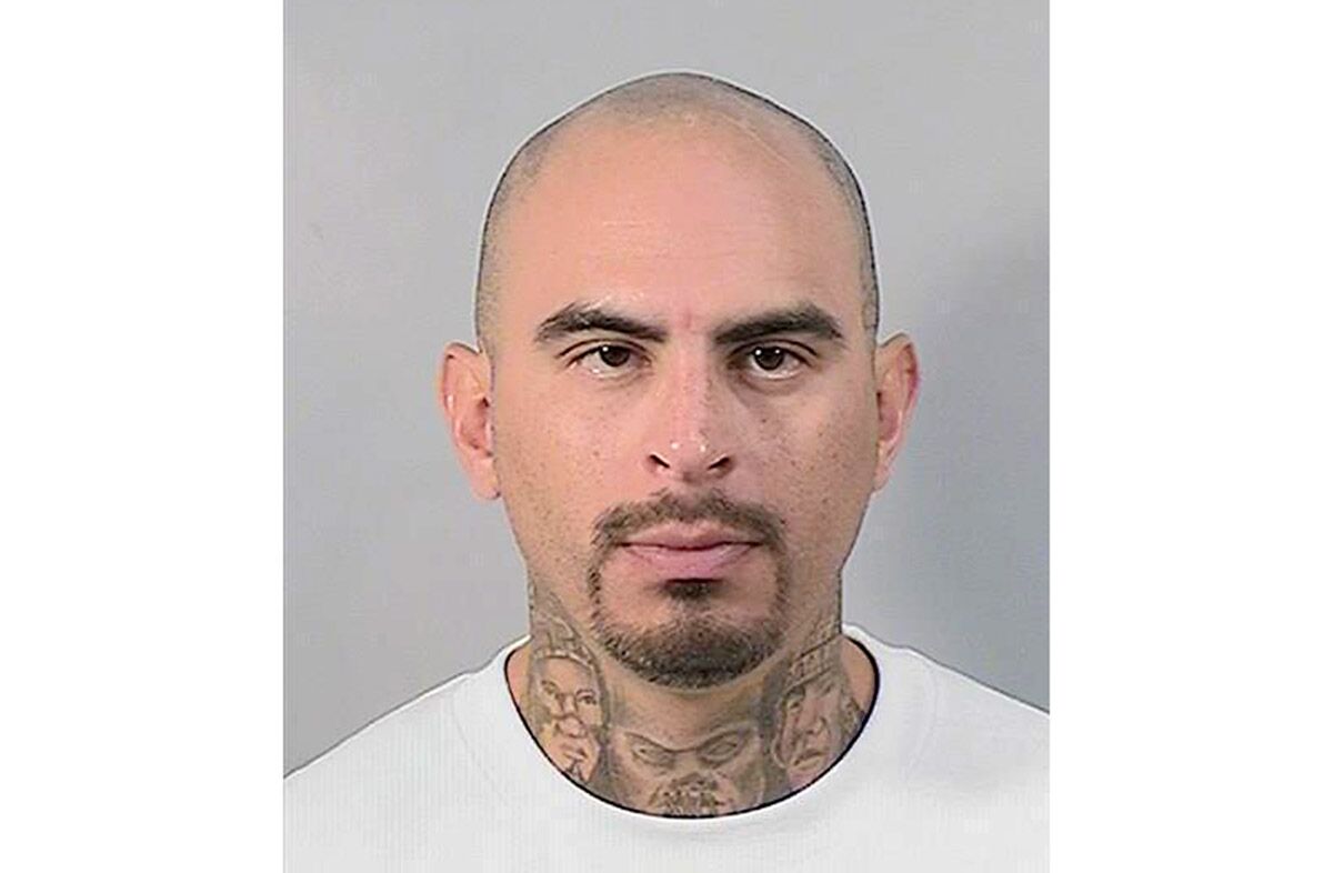A mugshot of a man with a shaved head, goatee and neck tattoos.