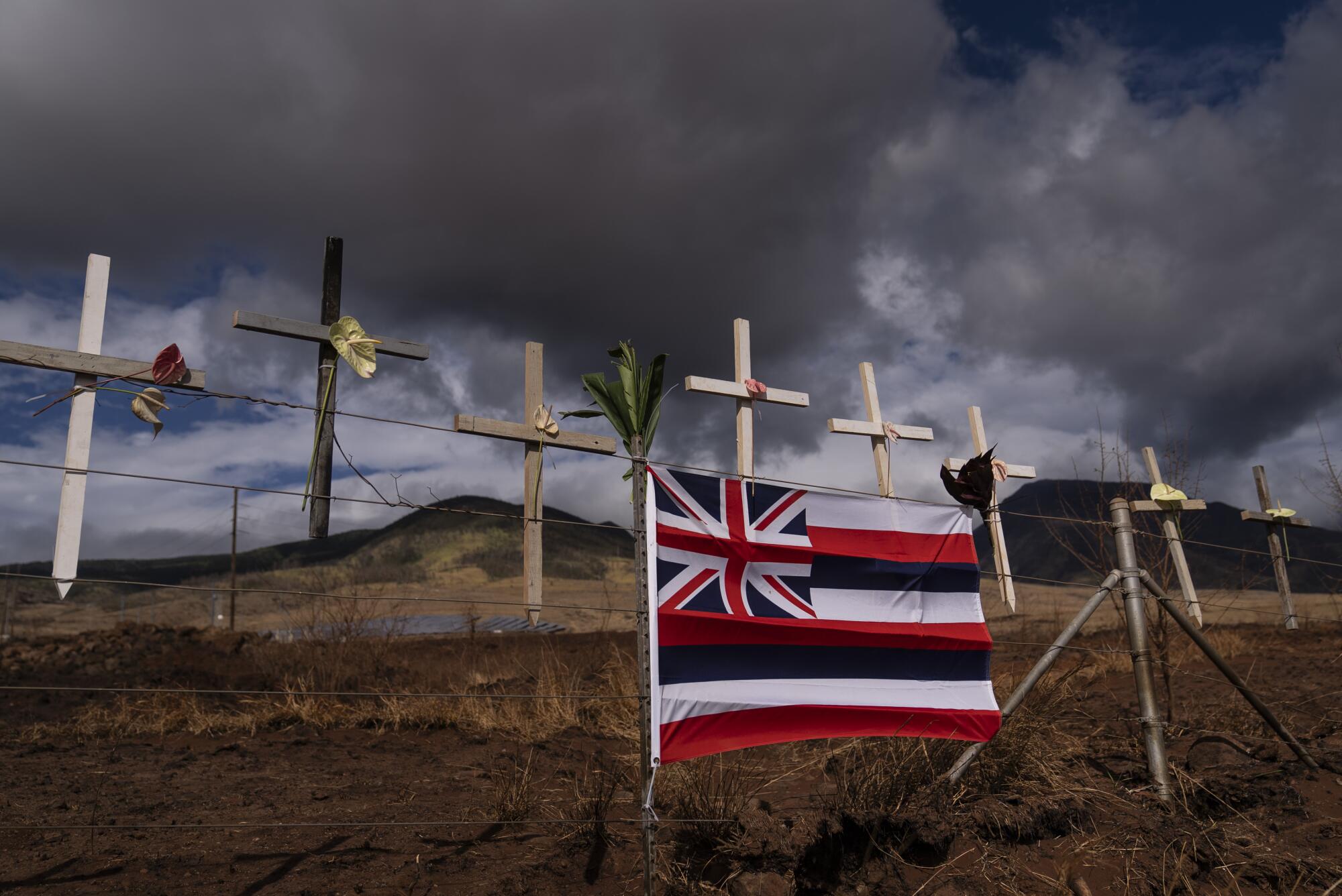 Crosses and a flag with a mini-Union Jack and white, red and blue stripes stand along a brown roadway 