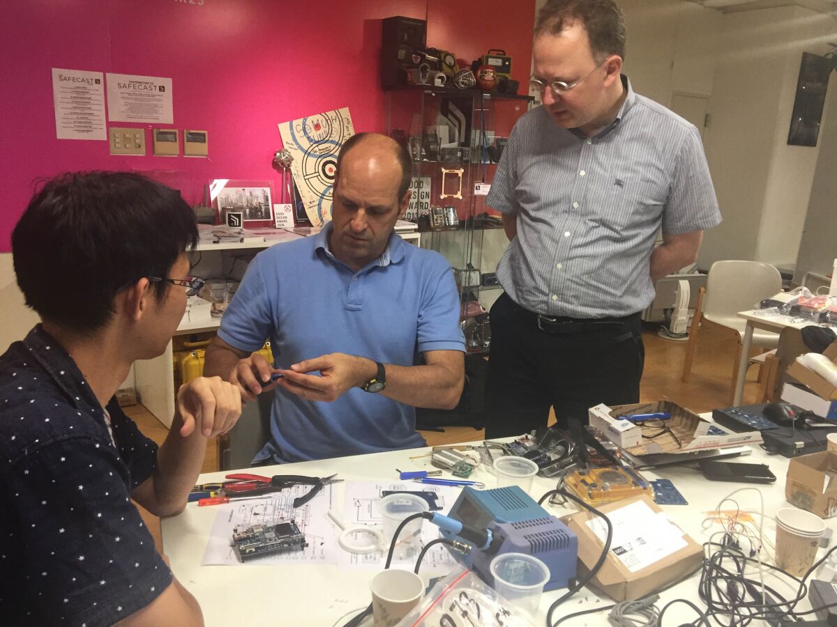 Joe Moross, center, and Pieter Franken, right, teach Kohei Matsushita how to assemble one of Safecast's Geiger counter kits at the group's Tokyo office on July 6, 2016.