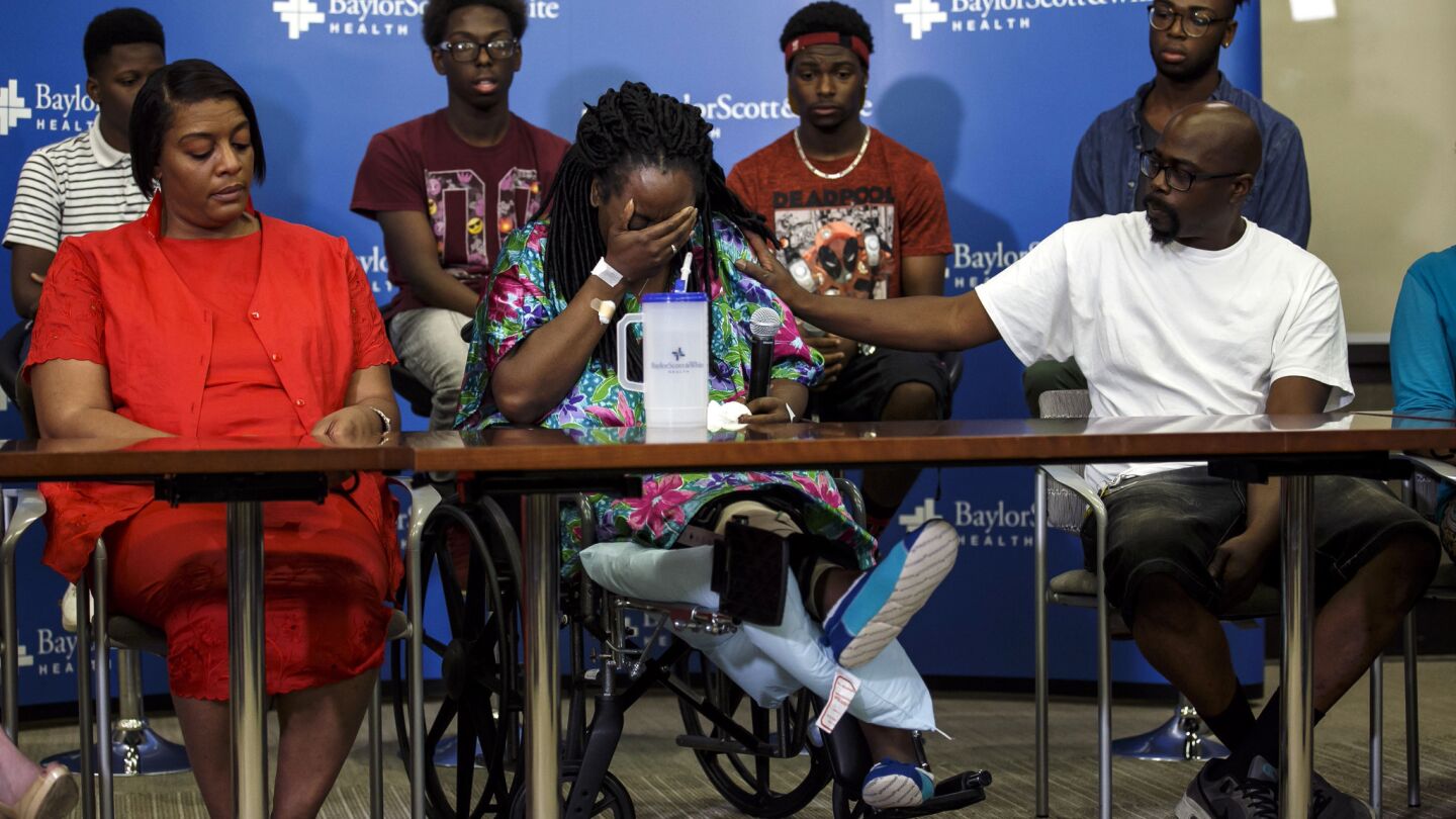 A wounded Shetamia Taylor, center, tears up as she recalls the Dallas police officers who saved her after she was wounded during a sniper attack Thursday night in which five officers were killed. At the news conference at a Dallas hospital, Taylor is surrounded by her sister, Teresa Williams, her husband, Lavar Taylor, and her children behind her.