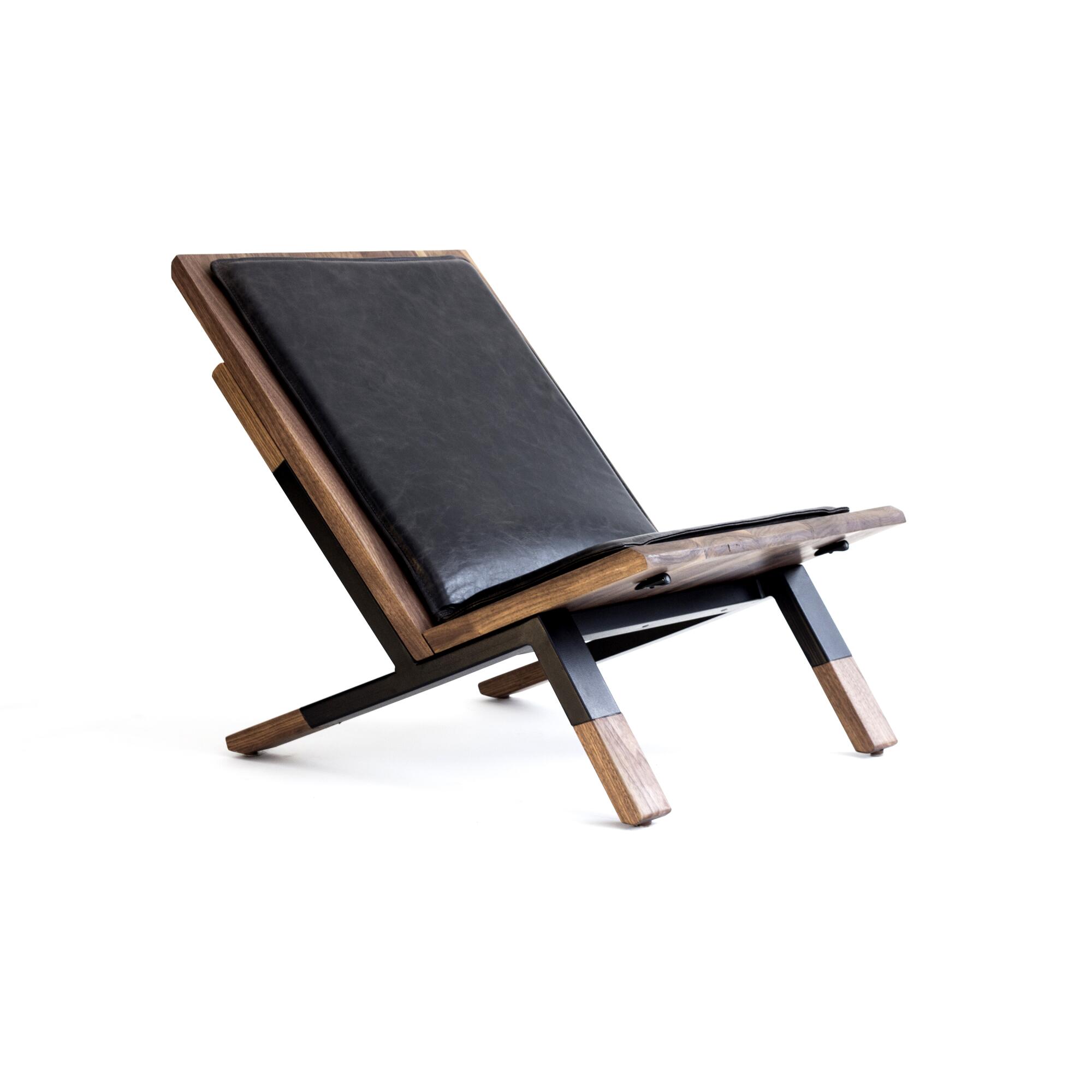 A low-slung chair made with stained wood and black leather is shown against a white background.