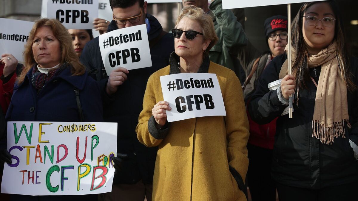 Supporters of the Consumer Financial Protection Bureau hold signs as they protest in front of the agency in November against President Trump's appointment of Mick Mulvaney as acting director.