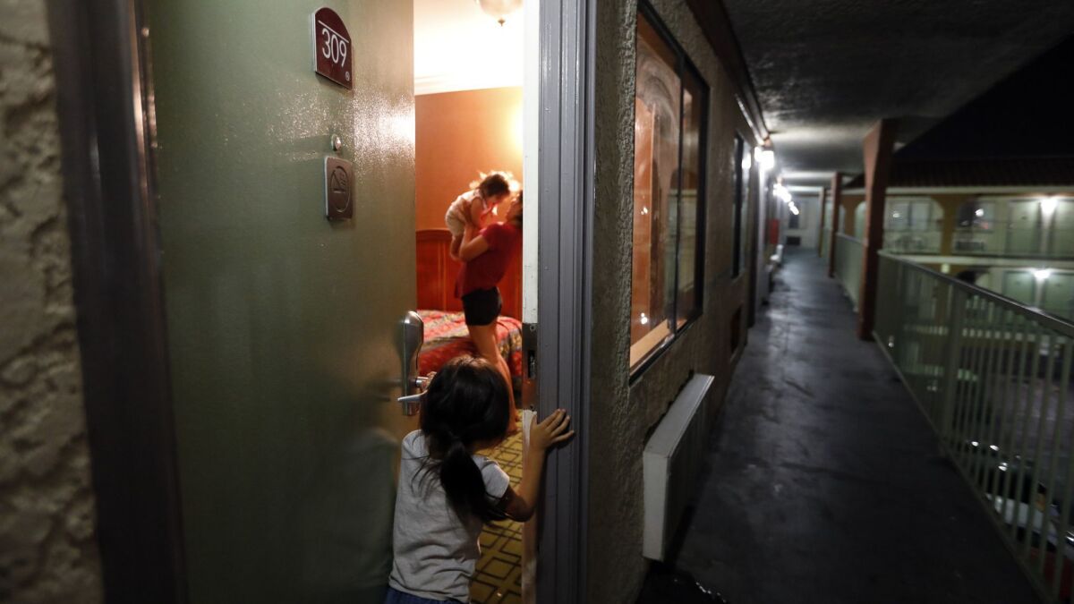 Madelyn, 5, peeks into the motel room where her family is staying in North Hills. Madelyn's mother, Brenda Salgado, 29, holds Mayla, 1.