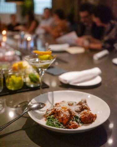 A dish of spaghetti in a meat sauce with a cocktail on a wood table