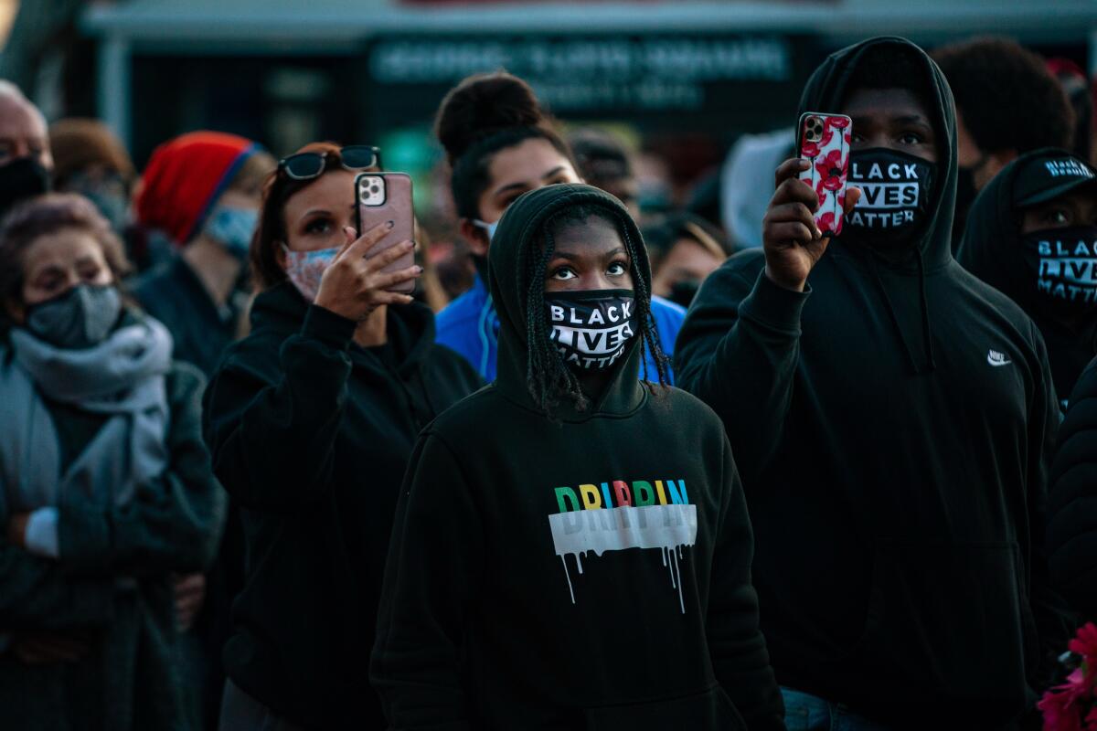 people gathered together, holding up cellphones and wearing masks