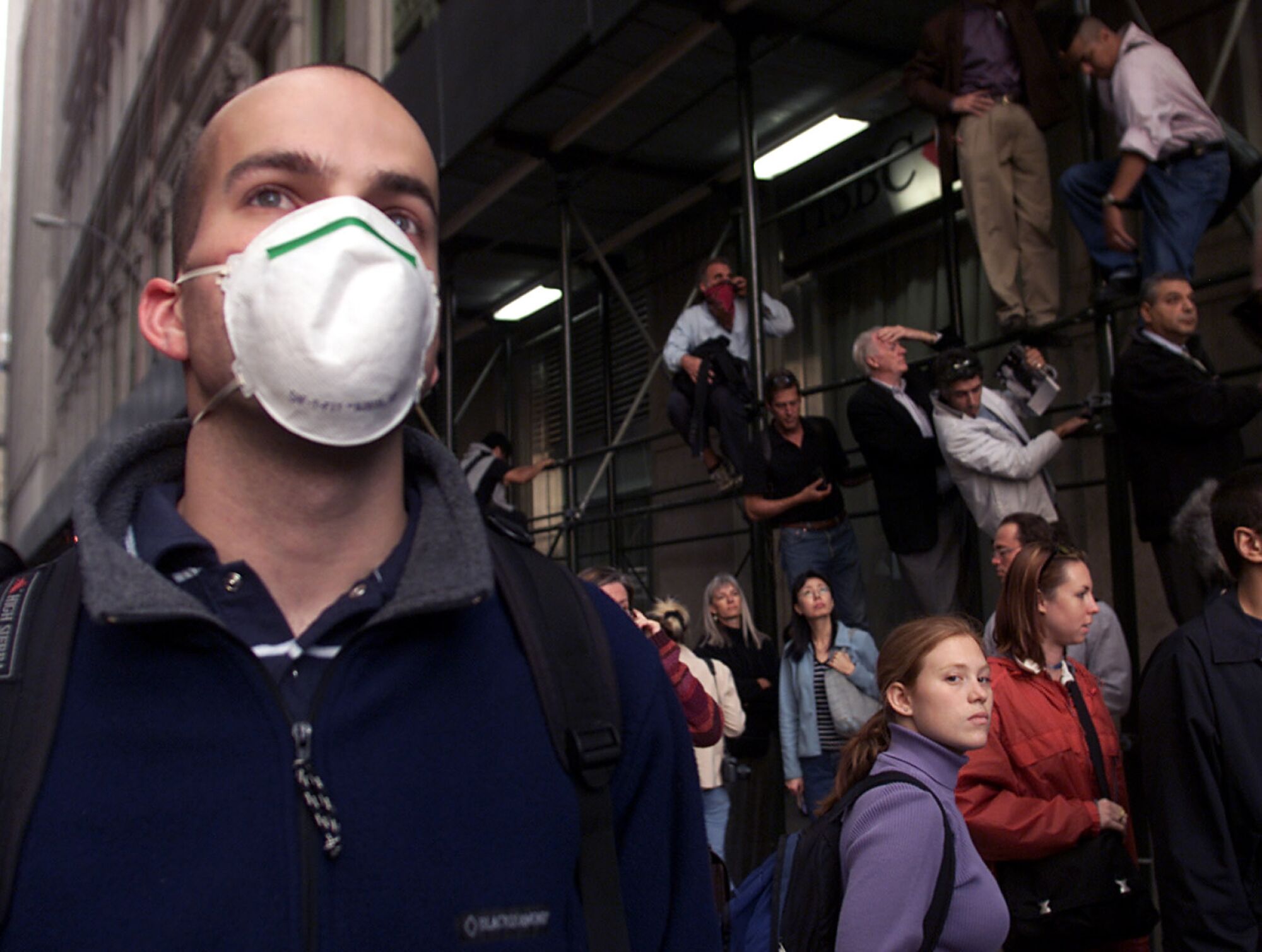 A man in a protective mask stands next to a group of onlookers