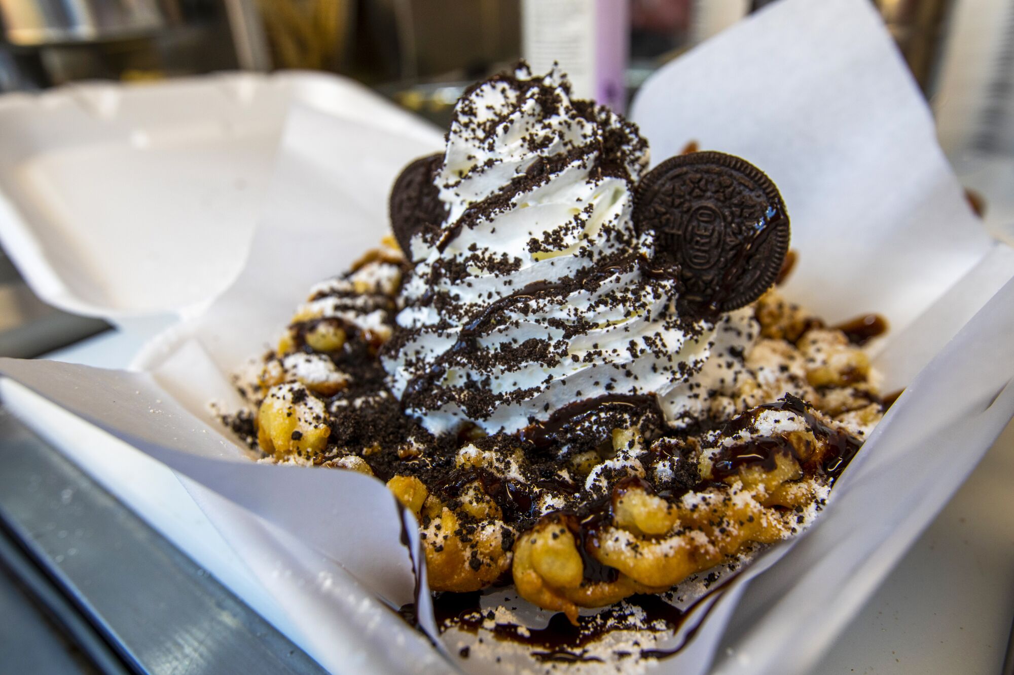 A funnel cake topped with whipped cream and Oreos.