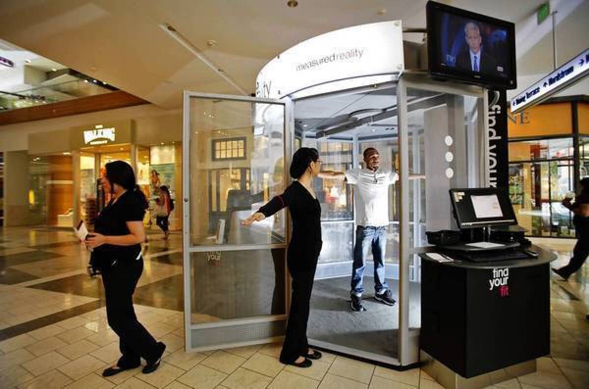 Sandra Garcia, left, the station manager at the Me-Ality sizing machine in the Westfield Topanga mall, helps Quincy Thomas, 19, get into position before the machine scans him.