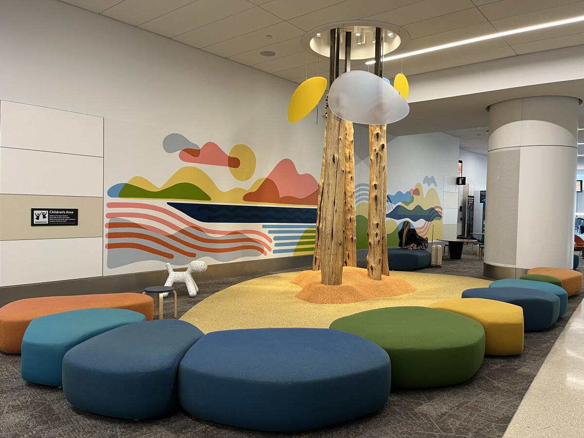 Tree limbs rise from a play area with cushioned ground, with multicolored benches and a colorful mural.