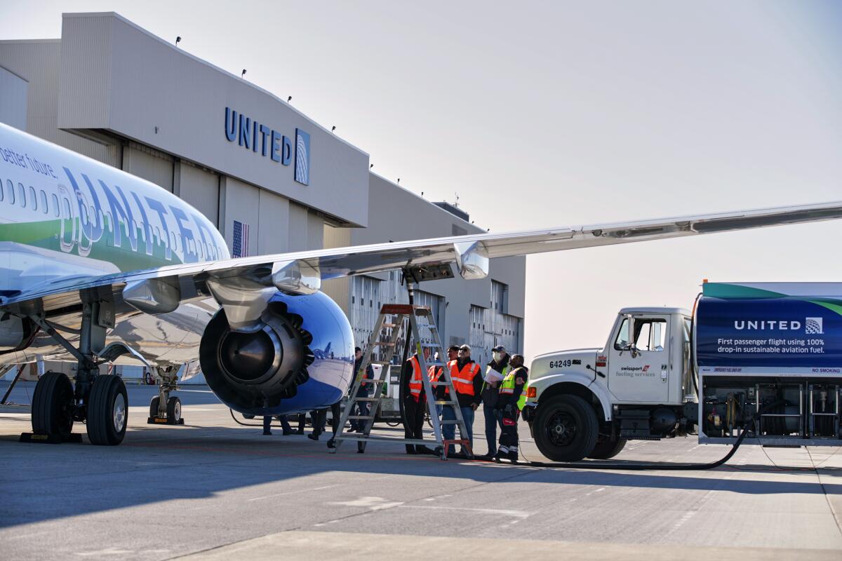 A group of workers stand under the wing of a United Airlines jetliner.