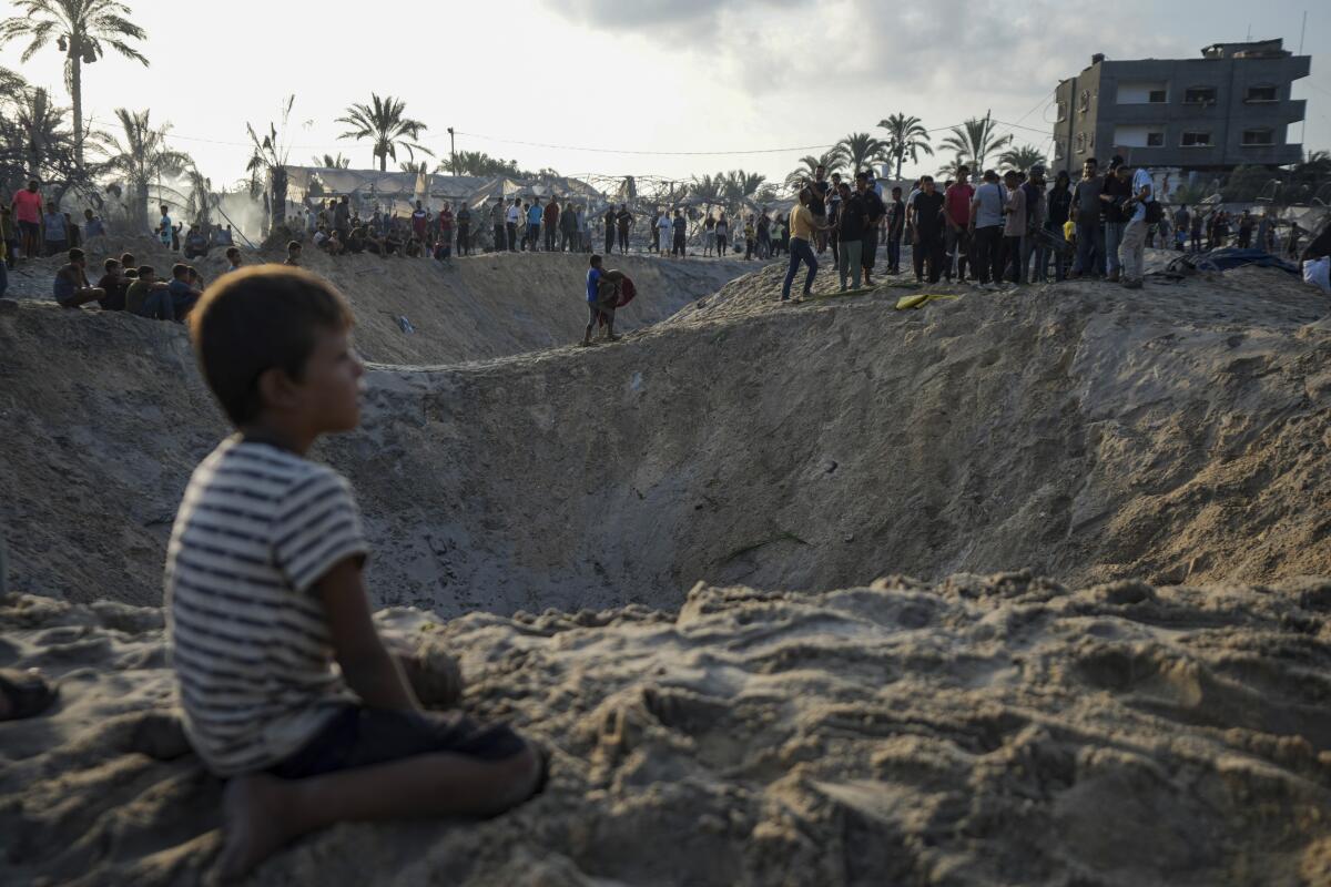 A child sits next to a crater in Gaza.