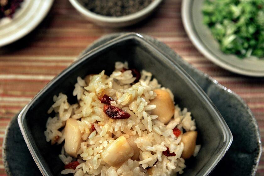 Spicy rice with scallops is flavored with sesame oil, soy sauce and sake and garnished with peppers, sesame seeds, chives and yuzu.
