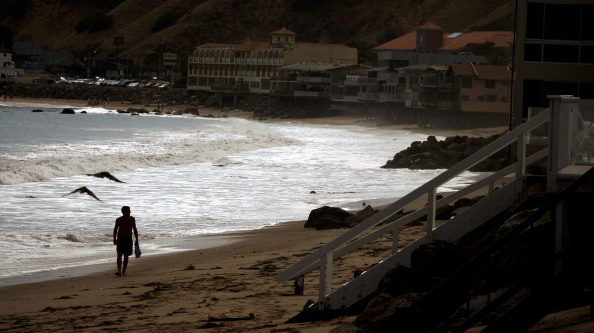 A beachgoer walks along Carbon Beach in Malibu, also known as "Billionaires' Beach." The Malibu Beach Inn is seen in the left background.