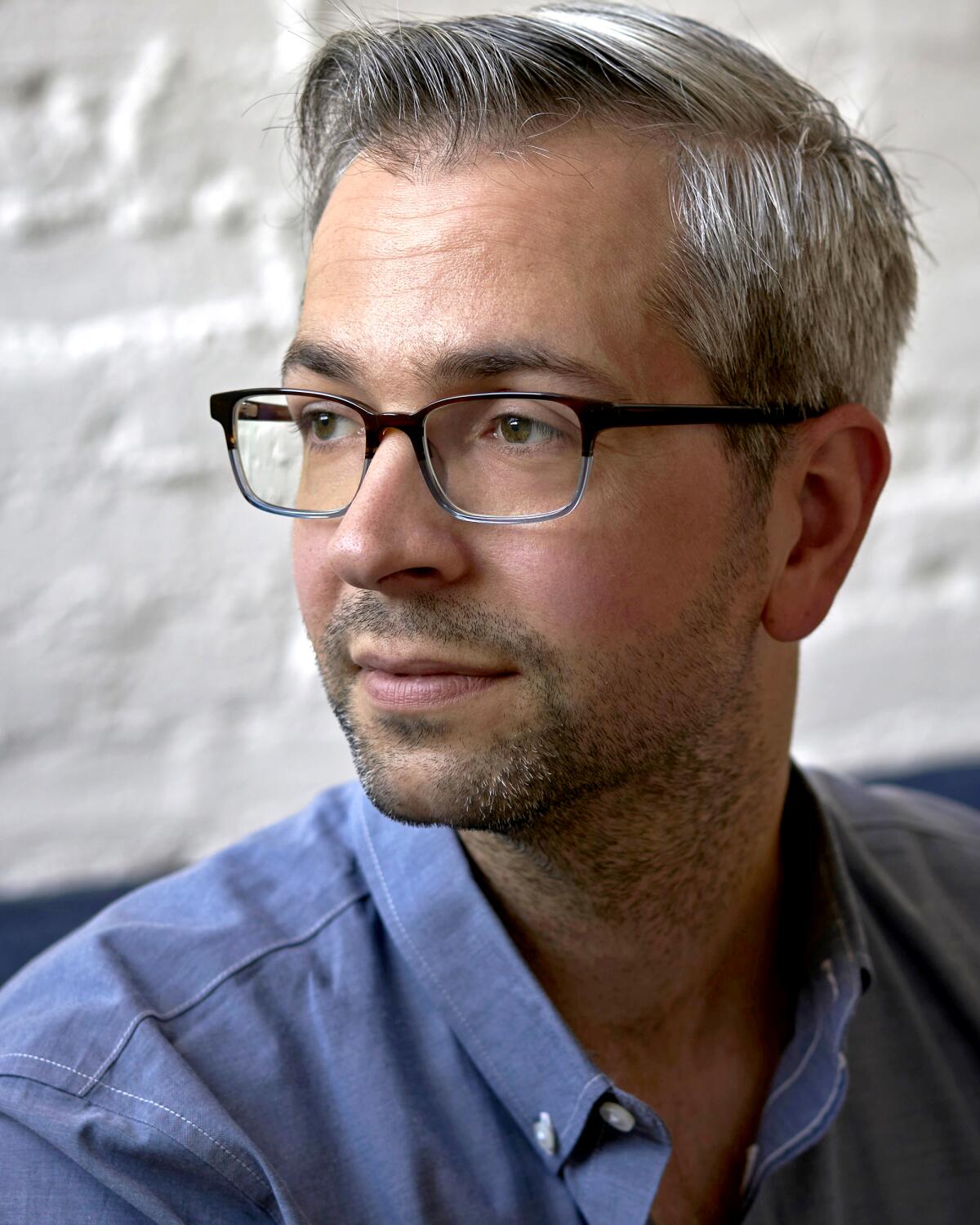 A portrait of a writer with close-cropped salt-and-pepper hair, wearing plastic-rimmed glasses.